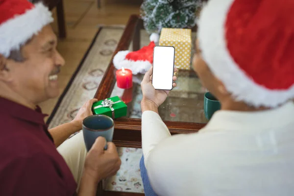 スマートフォンのクリスマスビデオ通話を作るサンタの帽子の幸せな出産の大人の息子と高齢者の父親 クリスマスやお祭りや通信技術は — ストック写真