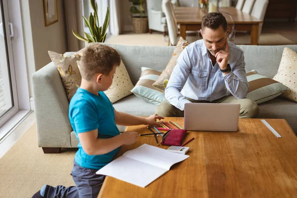 息子が家で宿題をしている間 ノートパソコンを使っている白人の父親 家庭教育とコロナウイルス感染症の概念の間の自宅からの作業 — ストック写真
