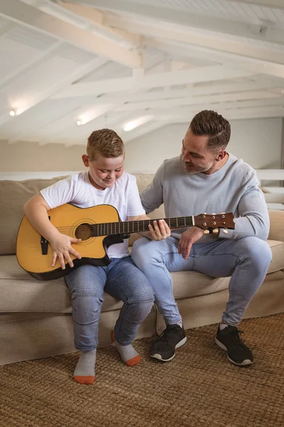 白人の父は息子に自宅でソファに座ってギターを弾くように教えている 幼少期と趣味の概念 — ストック写真