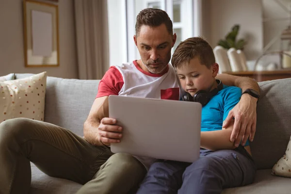 白种人的父亲和儿子坐在家里的沙发上使用笔记本电脑 技术和家庭观念 — 图库照片