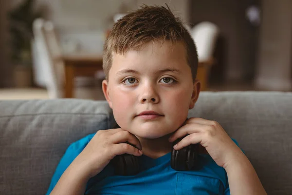 一个带着耳机坐在家里沙发上的高加索男孩的画像 技术和家庭概念 — 图库照片