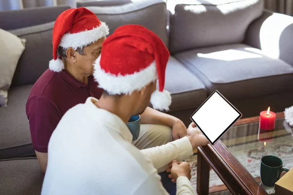 サンタの帽子の出産の大人の息子と高齢者の父親は タブレットクリスマスビデオ通話を行います クリスマスやお祭りや通信技術は — ストック写真