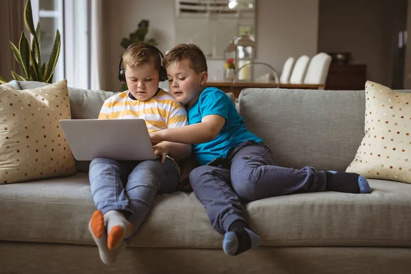 两个高加索男孩坐在家里的沙发上 用笔记本电脑 技术和家庭概念 — 图库照片