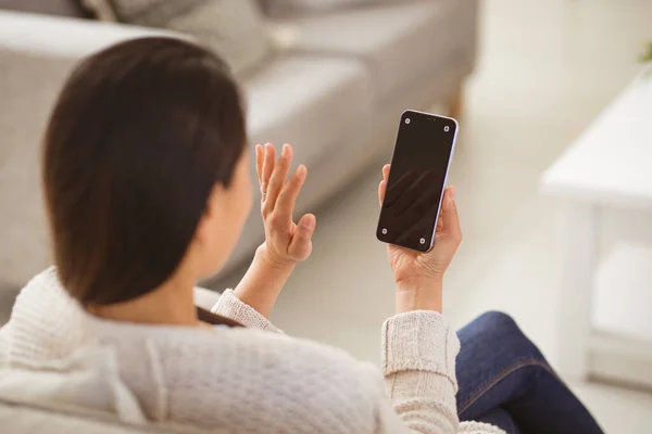 画面上にコピースペースのあるスマートフォンでビデオ通話をしているアジアの女性のバックビュー テクノロジーで家でリラックスして — ストック写真