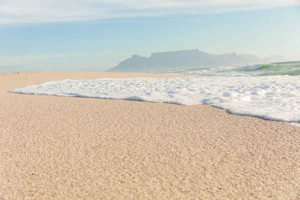 海面上的海浪泡沫在阳光灿烂的海滩上飘扬 背景远近群山 自然美 — 图库照片