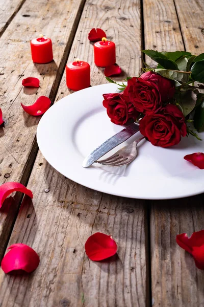 新鲜的红玫瑰和餐具在盘子里 用蜡烛放在木制桌子上 复制空间 情人节 花与爱情的概念 — 图库照片