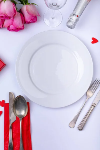 テーブルの上にボトルと刃物でピンクのバラに囲まれた空の白いプレート 愛とバレンタインの食事をコピースペースで — ストック写真