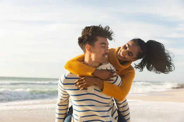 Biracial Muž Dává Šťastný Přítelkyně Piggyback Jízda Pláži Proti Obloze — Stock fotografie