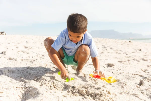 晴れた日にビーチで砂やおもちゃで遊んでいる間にうずくまっている鳥の男の子の完全な長さ 子供時代と週末 — ストック写真