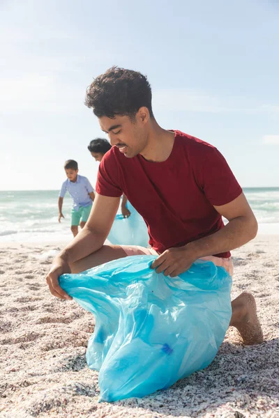 Biracial Man Kneeling While Collecting Garbage Blue Plastic Bag Sky — Stock Photo, Image