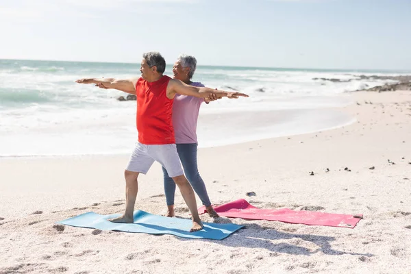 帮助有战士的男子在海滩上对着天空练习瑜伽时 这位年长的比利西亚女子摆出瑜伽姿势 积极的生活方式和健身 — 图库照片