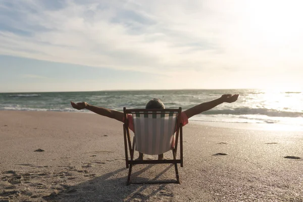 日没の間にビーチで折りたたみ椅子に座って腕を伸ばして引退したシニアの出産の男 ライフスタイルと週末 — ストック写真