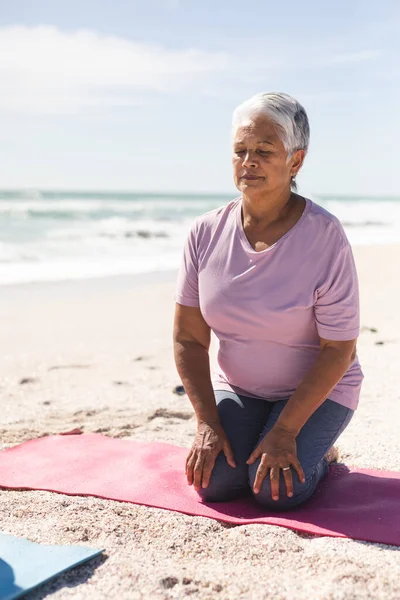 在阳光普照的海滩上跪在瑜伽垫上 眼睛闭着沉思的伯明翰老年妇女 积极的生活方式和健身 — 图库照片