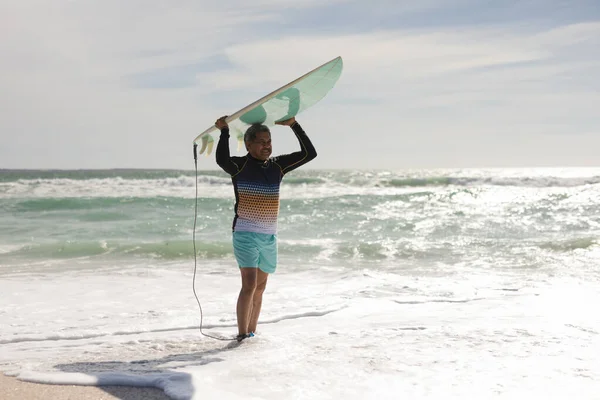Biracial Homem Sênior Carregando Prancha Surf Sobre Cabeça Enquanto Praia — Fotografia de Stock