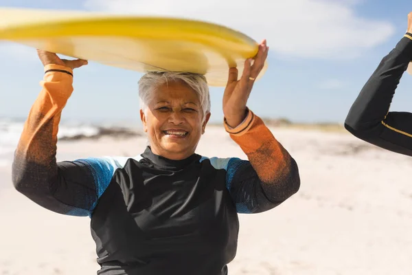在阳光普照的海滩上 一位面带微笑的退休老年妇女头戴冲浪板的画像 水上运动和积极的生活方式 — 图库照片