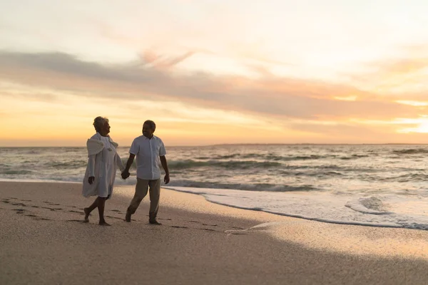 ビーチで夕日を楽しみながら海岸を歩いて手を握っているシニア多人種カップルの完全な長さ ライフスタイル愛週末 — ストック写真