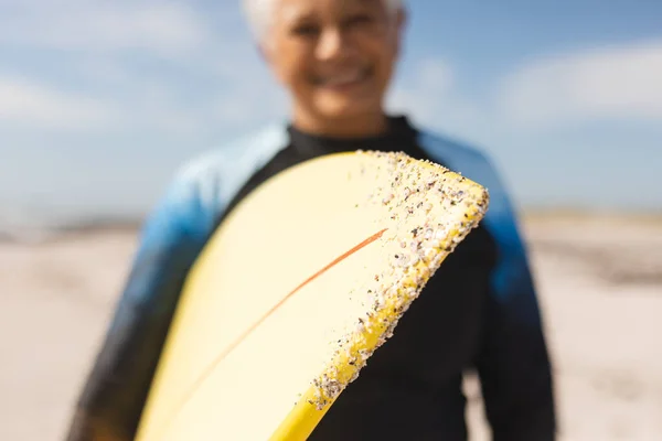 晴れた日にビーチで出産の先輩女性が笑顔で開催された砂でサーフボード ウォータースポーツやアクティブライフスタイル — ストック写真