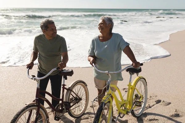 Casal Sénior Multirracial Feliz Falando Enquanto Roda Bicicletas Praia Durante — Fotografia de Stock