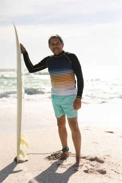 空に対して日当たりの良いビーチでサーフボードに立っている出産の先輩の完全な長さの肖像画 ウォータースポーツやアクティブライフスタイル — ストック写真