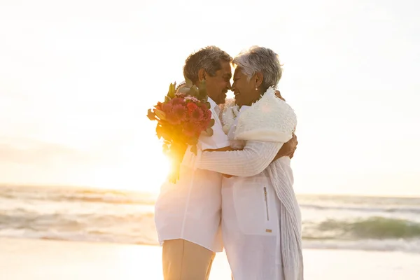 Šťastný Novomanželský Senior Multiracial Pár Objímání Při Držení Kytice Pláži — Stock fotografie