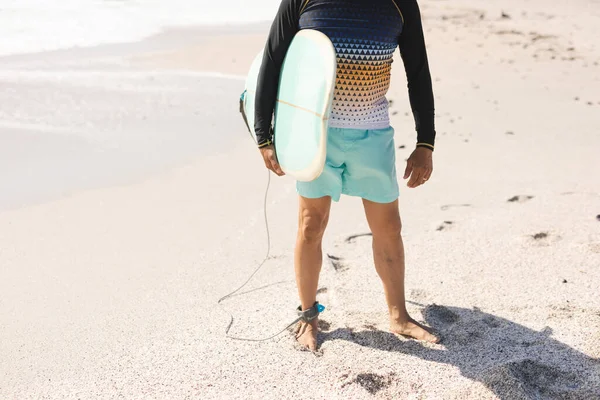 日当たりの良いビーチで海岸に立ってサーフボードを保持する男の低セクション ウォータースポーツやアクティブライフスタイル — ストック写真