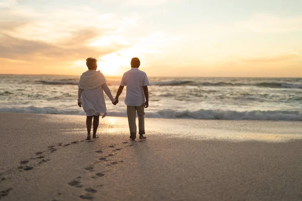 日没時にビーチを歩いて手をつないで新婚の多人種シニアカップルの背面ビュー ライフスタイル愛週末 — ストック写真