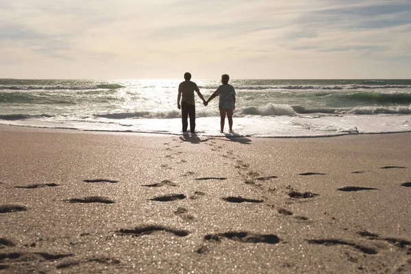 阳光明媚的日子里 多种族的老夫妇手牵手站在海滩上 在沙滩上留下脚印 生活方式 爱情和周末 — 图库照片