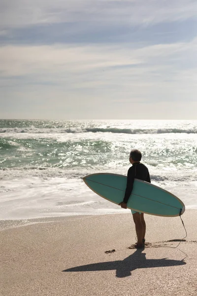 Biracial Senior Hombre Llevando Tabla Surf Mirando Salpicaduras Olas Mar — Foto de Stock