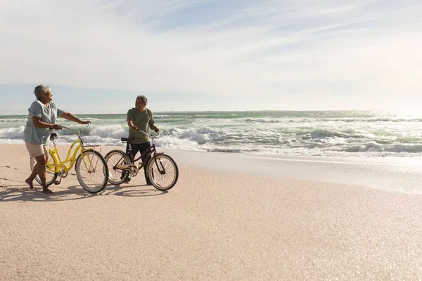 Senior Multiracial Couple Talking While Wheeling Bicycles Shore Sunny Beach — Stock Photo, Image