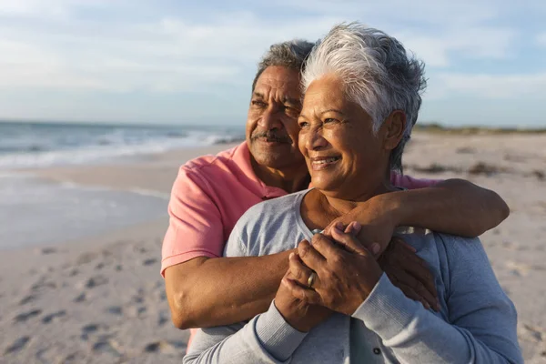 日没の間にビーチを眺めながら抱き合う思慮深い高齢者の多人種カップル ライフスタイル愛週末 — ストック写真