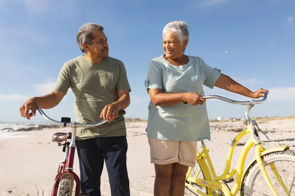 Багаторасова Старша Пара Дивиться Один Одного Стоячи Велосипедами Сонячному Пляжі — стокове фото