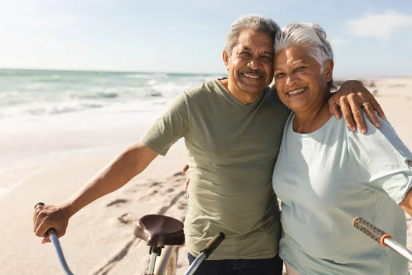 晴れた日にビーチで自転車の周りに腕を持つ高齢者の多人種のカップルの笑顔の肖像画 活動的な生活と交通機関 — ストック写真