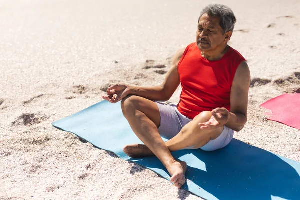 Biracial Senior Mann Mit Geschlossenen Augen Meditiert Auf Yogamatte Sonnigen lizenzfreie Stockbilder