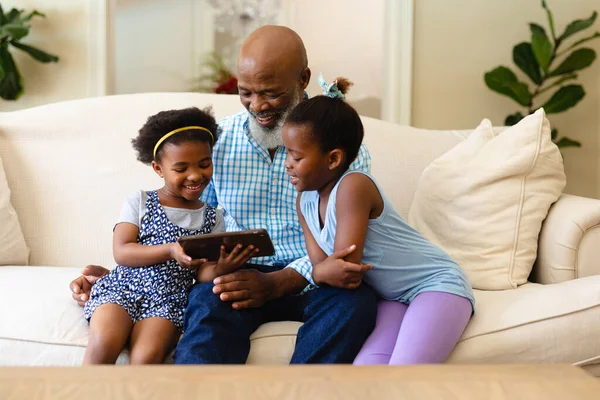 アフリカ系アメリカ人の祖父と彼の2人の孫娘は自宅でデジタルタブレットを使用しています 家族愛技術の概念を変えずに — ストック写真
