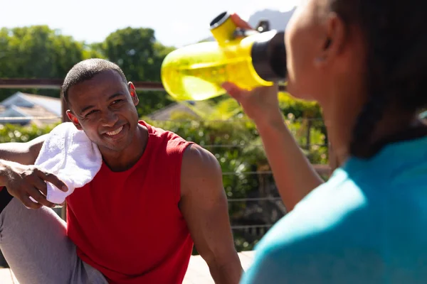 Smiling African American Man Watching Girlfriend Drinking Water Bottle Sunny — Stock Photo, Image