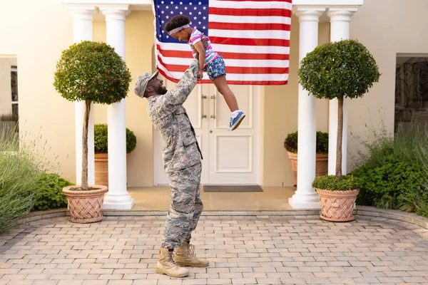 快乐的非裔美国军人父亲抱着高傲的女儿与美国国旗在屋前 团结和爱国主义 — 图库照片