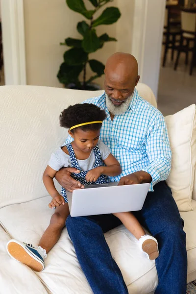アフリカ系アメリカ人の祖父と孫娘がノートパソコンを持って家のソファに座っている 家族愛技術の概念を変えずに — ストック写真