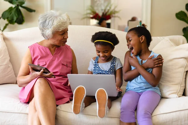アフリカ系アメリカ人の祖母と彼女の2人の孫娘は 自宅のソファに座ってラップトップを使用しています 家族愛技術の概念を変えずに — ストック写真
