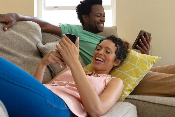 Jovem Casal Multirracial Alegre Usando Smartphones Enquanto Relaxam Juntos Sofá — Fotografia de Stock