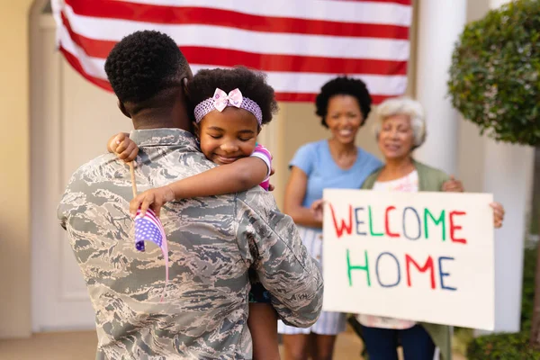 Smiling african american girl embracing soldier father on his return with family in background. family, bonding and patriotism, unaltered.