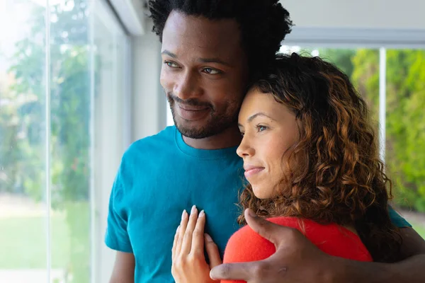 Romantiskt Multietniskt Par Omfamnar Samtidigt Som Tittar Genom Fönstret Tillsammans — Stockfoto