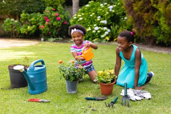 Sonriente Chica Afroamericana Arrodillada Por Hermana Regando Planta Jardín Concepto —  Fotos de Stock