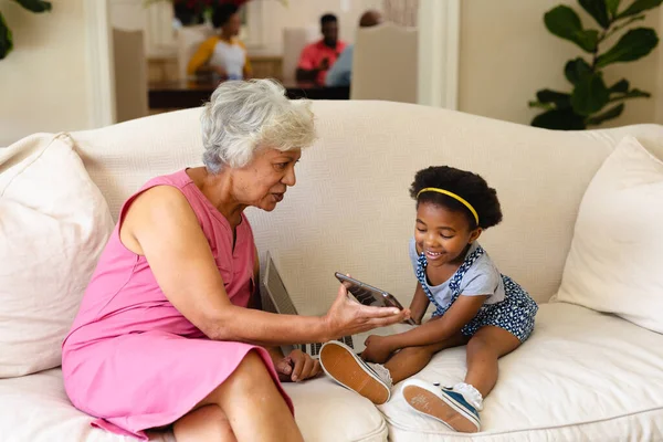 自宅のソファに座っている孫娘にデジタルタブレットを示すアフリカ系アメリカ人の祖母 家族愛と団結の概念を変えずに — ストック写真