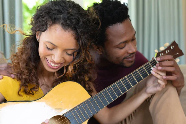 アフリカ系アメリカ人の男性は 自宅で一緒に座っている間 出産のガールフレンドにギターを教えています 人々や音楽の概念を変えずに — ストック写真