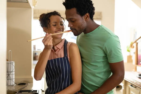 自宅で料理をしながら アフリカ系アメリカ人の彼氏に食べ物を味わう若い出生女性を笑顔 人々や料理の概念を変えずに — ストック写真