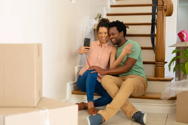 一对快乐的多种族的年轻夫妇坐在楼梯上 在新家自理 重新安置和技术概念 — 图库照片