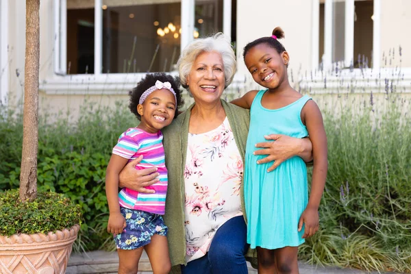 アフリカ系アメリカ人の祖母の笑顔と彼女の孫娘を屋外で抱きしめる肖像画 家族愛と団結の概念を変えずに — ストック写真