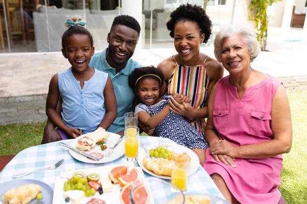 裏庭のブランチ中にダイニングテーブルに座っているアフリカ系アメリカ人の家族の笑顔の肖像画 家族愛と団結の概念を変えずに — ストック写真