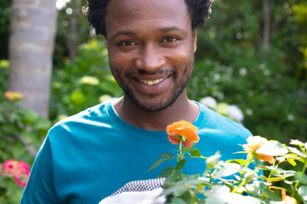 Retrato Joven Afroamericano Sonriente Sosteniendo Una Planta Con Flores Mientras —  Fotos de Stock