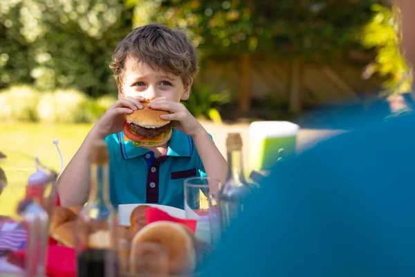 白人の少年は庭のテーブルで家族と一緒に座ってバーガーを食べています 週末のライフスタイルの概念は — ストック写真